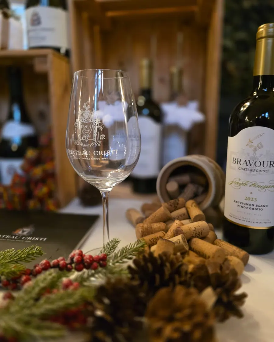 An empty Château Cristi tasting glass on a table set for a tasting, beside a bottle and a bowl of corks